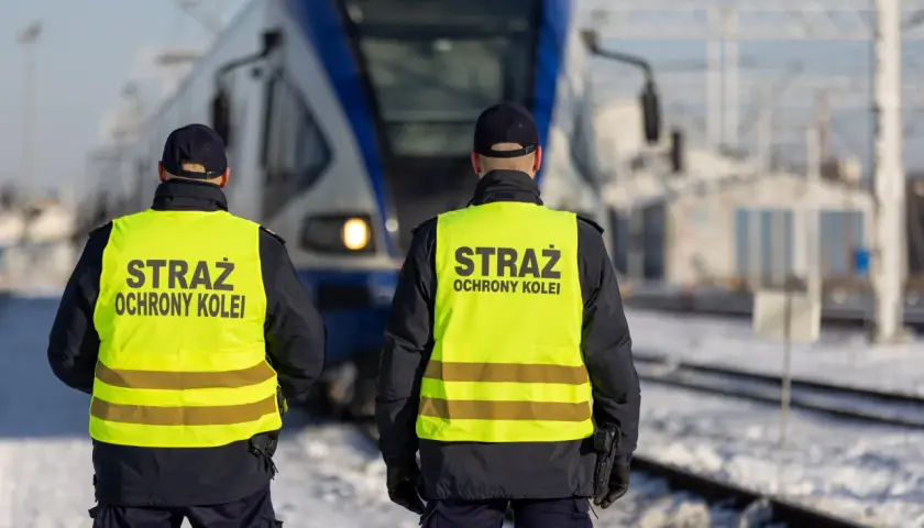 Dwóch funkcjonariuszy Straży Ochrony Kolei w kamizelkach odblaskowych stoi przed pociągiem. Czy mogą wystawić mandat?