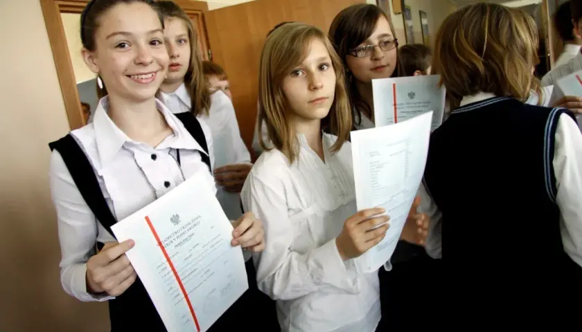 Uczennice z dyplomami, jedna z nich uśmiecha się, zastanawiając się, jaka średnia na czerwony pasek w 4 klasie.
