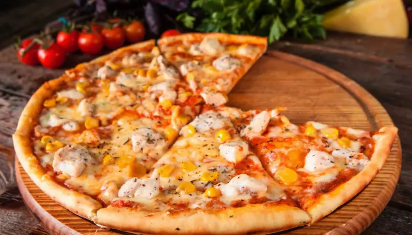 Pyszna pizza z kurczakiem i kukurydzą, podana na drewnianej desce, z pomidorkami koktajlowymi i bazylią w tle.