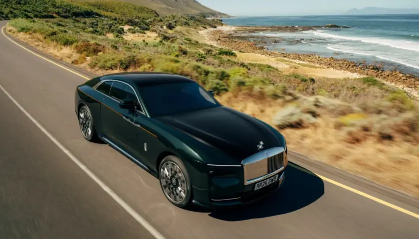Elegancki, ciemnozielony Rolls-Royce elektryczny sunie po malowniczej drodze nad oceanem.