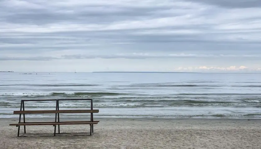 Pusta ławka na plaży w Gąskach, wpatrzona w spokojne morze pod zachmurzonym niebem.