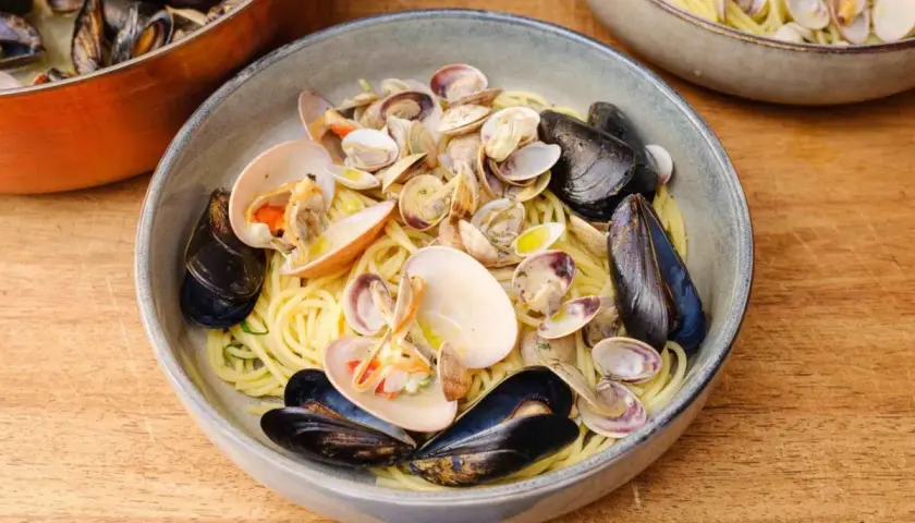 Spaghetti Vongole mit Muscheln und Venusmuscheln, serviert in einer Schüssel auf einem Holztisch.