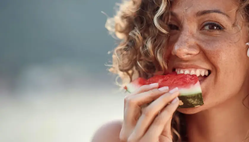 En glad kvinna med lockigt hår njuter av en saftig vattenmelon. Kanske en gravid kvinna som får sitt sug!