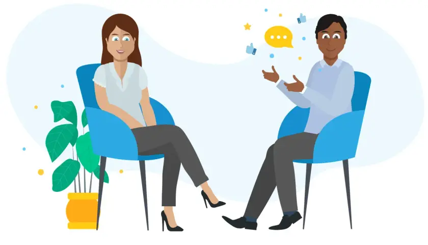 A man and woman sit in chairs, discussing. A speech bubble and thumbs-up icons suggest they are learning how to give feedback effectively.