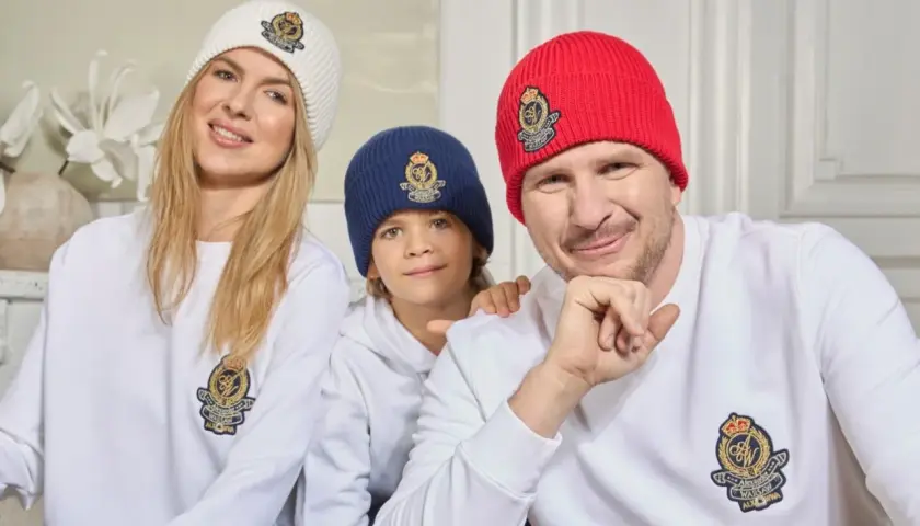 Filip Chajzer z rodziną w czapkach i bluzach z herbem. Uśmiechnięty tata, mama i ich dzieci.