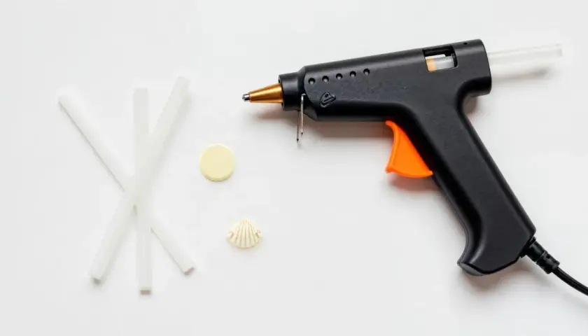 Pistolet do kleju na gorąco, kilka pałeczek kleju, muszelka i żółty krążek. Czy klej na gorąco przewodzi prąd?