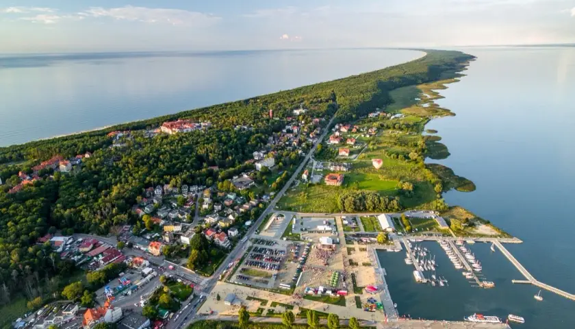 Widok z lotu ptaka na Krynicę Morską. Widać zalew, lasy, zabudowania i tętniący życiem rynek z mariną pełną łodzi.
