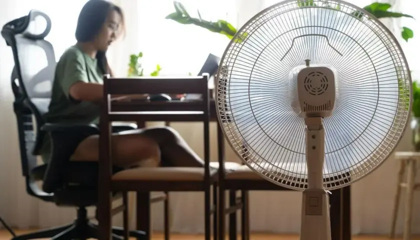 Kobieta pracuje przy biurku, a obok stoi wentylator pokojowy. Zastanawiasz się, ile prądu zużywa wentylator pokojowy?