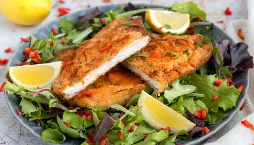 Knuspriges, low carb Putenschnitzel auf einem Salatbett mit Zitronenspalten und Paprikastückchen.