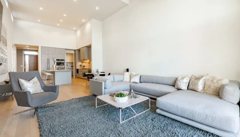 Nowoczesny salon z szarą sofą i fotelem, otwartą kuchnią i jadalnią. Idealne wnętrze do życia, jak w ofercie Vinci Immobilier Polska.