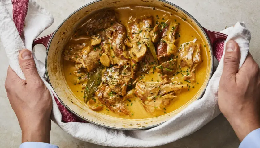Un plat de lapin à la moutarde crémeuse, garni de persil frais et de champignons, servi dans une cocotte en fonte.
