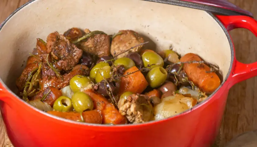Un savoureux sauté de veau aux olives, carottes et herbes aromatiques mijote dans une cocotte rouge.