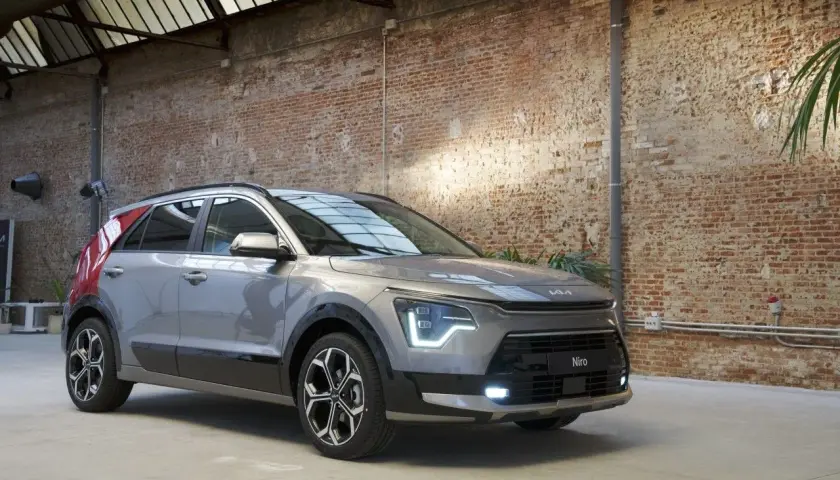 Un Kia Niro gris con detalles rojos en el pilar C, listo para una prueba. El coche está en un interior con paredes de ladrillo y techo acristalado.