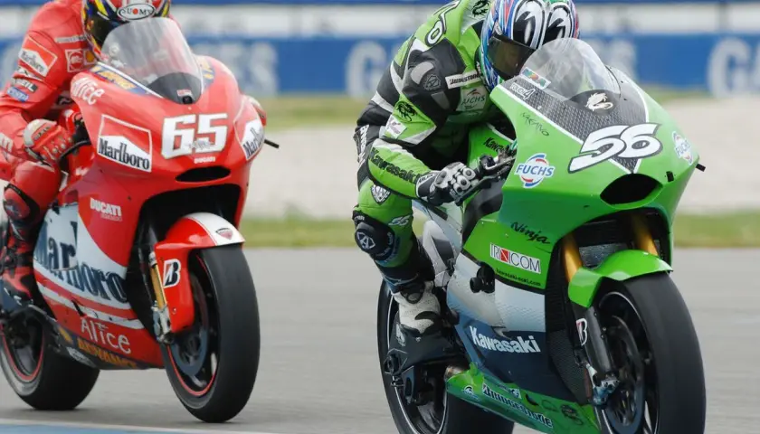 Piloto en moto verde Kawasaki compite en MotoGP, con el número 56. A su lado, otro piloto en rojo Ducati con el 65.