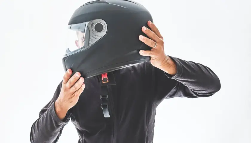 Persona indossa un casco nero, mostrando le sue parti. Le mani regolano il cinturino e la visiera.