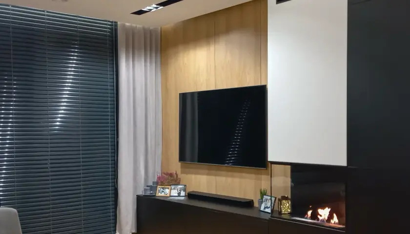Nowoczesny salon z telewizorem i palącym się kominkiem bio do zabudowy.