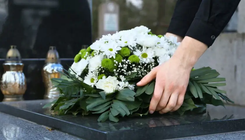 Dłonie układają wieniec na nagrobku. Czas żałoby w Kościele katolickim jest czasem refleksji i pamięci.