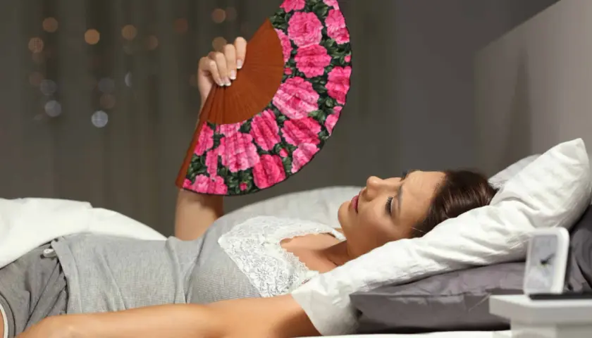 Donna a letto, insonne per il caldo, agita un ventaglio fiorato per combattere la sudorazione notturna.