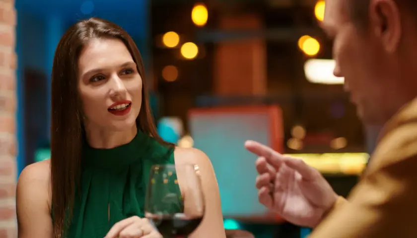 Kobieta w zielonej sukience i mężczyzna rozmawiają przy winie. Czy to przykład, czego nie robić na pierwszej randce?