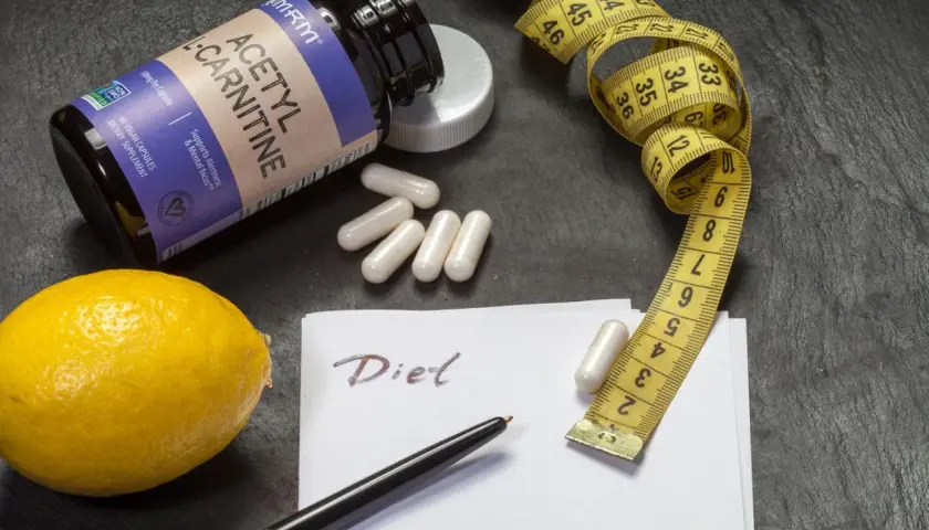 Flasche Acetyl-L-Carnitin, Maßband, Zitrone und Notiz "Diet". Die L-Carnitin Wirkung wird hier für eine Diät dargestellt.