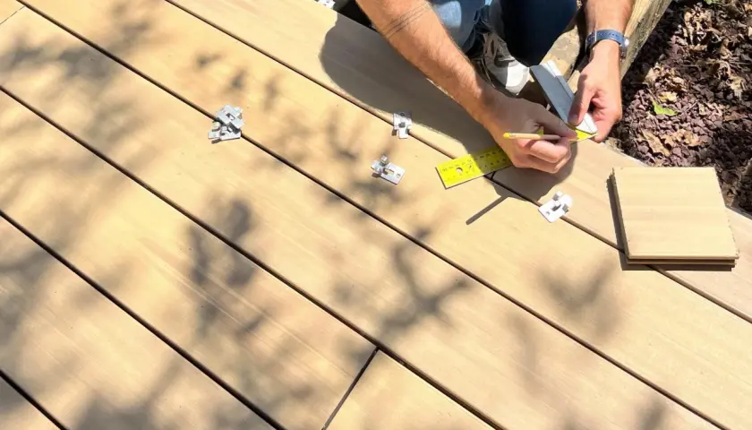 Pose d'une lame composite sur plot. Un artisan mesure avec une règle et un crayon pour une installation précise.