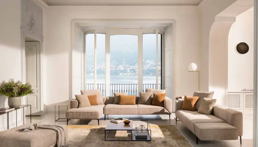 Salon lumineux avec canapé modulable, pouf et tapis doux pour une deco appartement cocooning parfaite. Vue sur lac et ville.