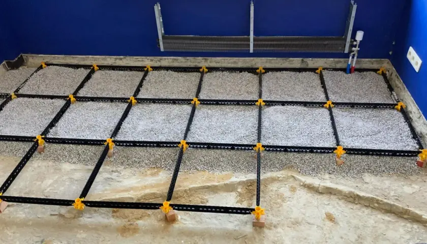 Vorbereitung für **OSB-Platten verlegen**: Ein Boden wird mit Schotter gefüllt und mit einem schwarzen Gitter und gelben Clips für den Trockenestrich vorbereitet.
