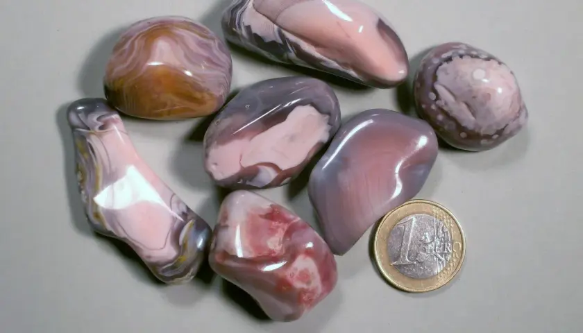 Glatt geschliffene Botswana Achat Steine in Rosa-, Grau- und Brauntönen, daneben eine 1-Euro-Münze.