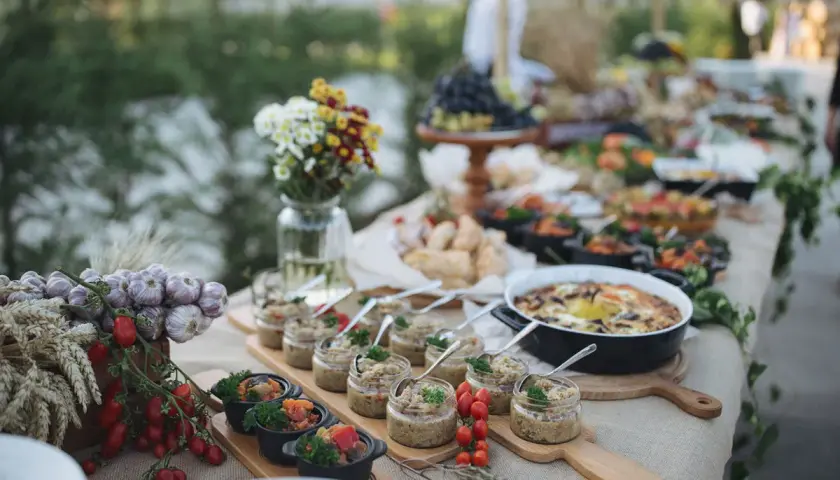 Un buffet baptême chic en extérieur, avec des verrines, des plats chauds et des décorations naturelles comme de l'ail et des tomates.