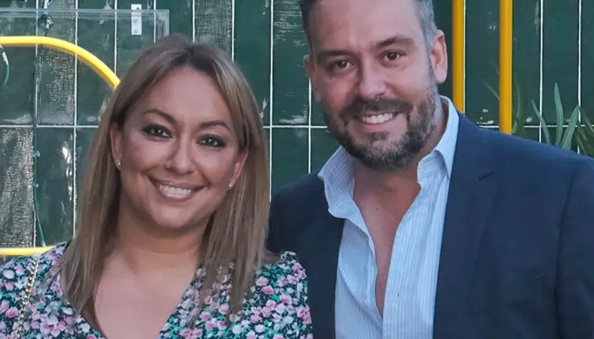 Kike Calleja y su pareja sonríen a la cámara. Ella lleva un vestido floral y él un traje azul.