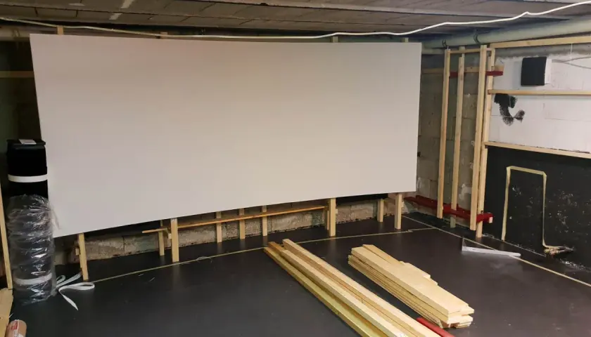 Große, weiße Leinwand für ein Heimkino, gestützt von Holzrahmen. Material für den **Beamer Leinwand selber bauen** liegt bereit.