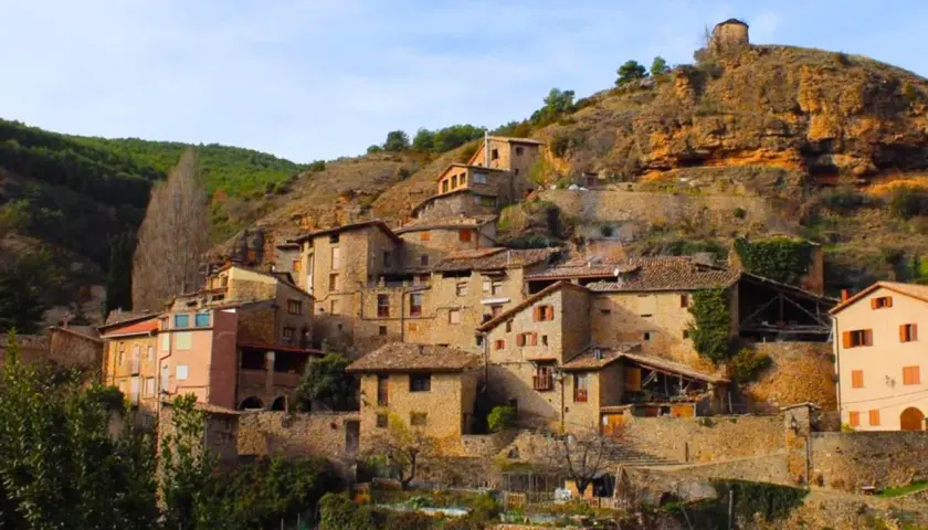 Un pintoresco senet de Barrabés se aferra a la ladera, con casas de piedra y tejados de teja bajo un cielo azul.