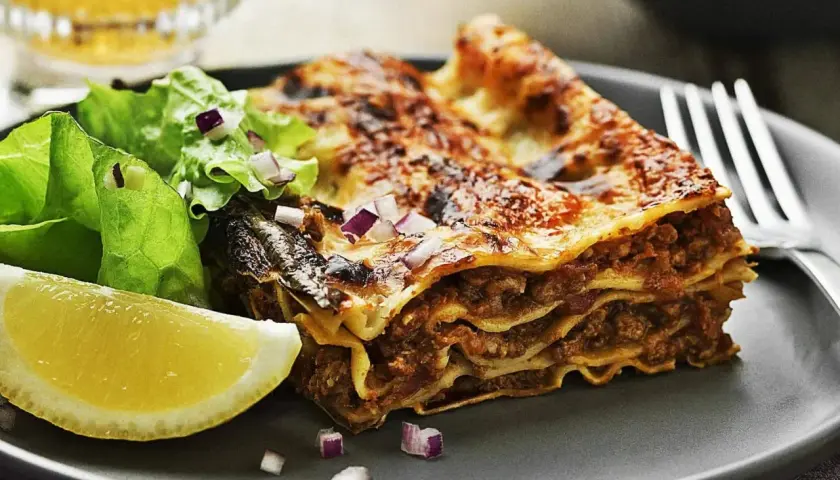En saftig bit lasagne med köttfärs och ost, serverad med en fräsch sallad och citronklyfta. Perfekt för lasagnens dag!
