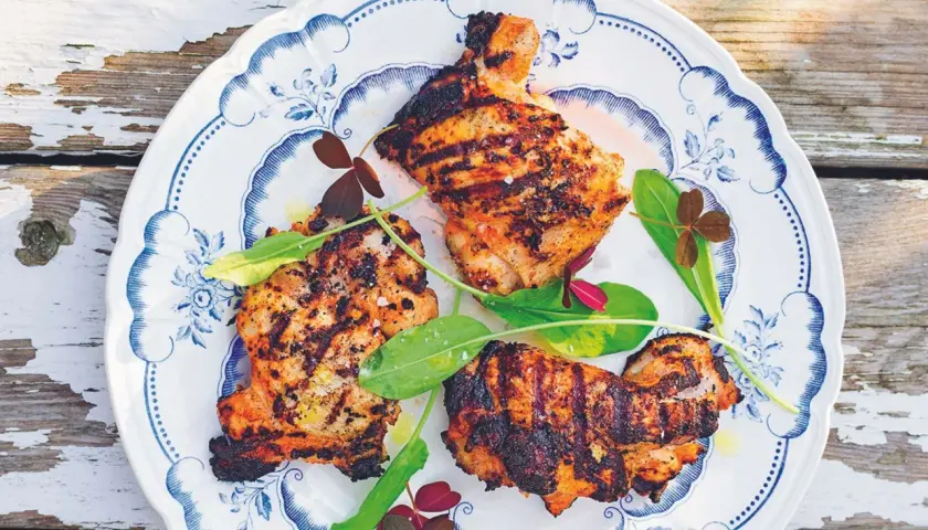 Grillad yoghurtmarinerad kyckling med gröna blad och klöver på en blåvit tallrik.