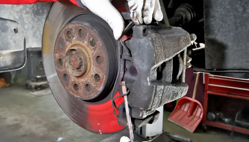 Mechanik w białych rękawiczkach dokonuje wymiany klocków hamulcowych, używając śrubokręta do podważenia starego klocka.