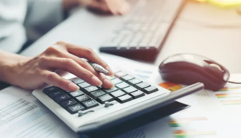 Dłoń z długopisem naciska klawisze kalkulatora, obok klawiatura i myszka. Analiza finansowa dla BNP Paribas Leasing.