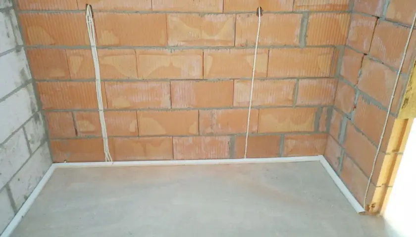Przewody w posadzce bez peszla, przygotowane do dalszych prac instalacyjnych. Widoczne puszki instalacyjne w ścianie z cegły.