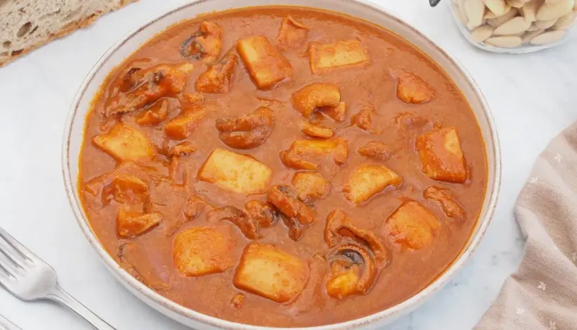 Un plato humeante de jibia en salsa, con trozos de patata y pan rústico al lado.