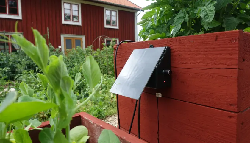 En solcellsdriven bevattning sköter om växterna vid ett rött hus.