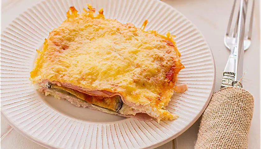 Porción de pastel de berenjenas gratinado con queso dorado, servido en plato blanco.