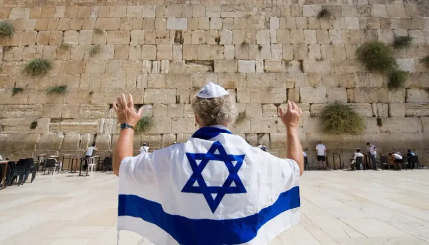 Mann mit israelischer Flagge und Davidstern betet an der Klagemauer, ein Ort des Judentums in Israel.