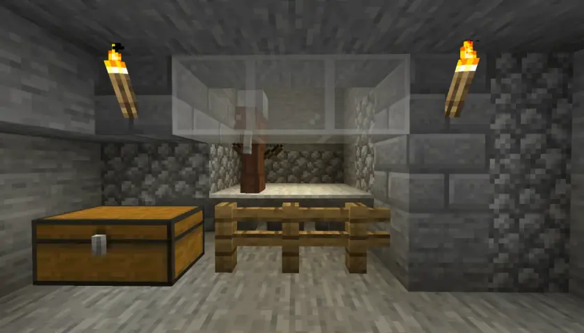 W klatce z Minecrafta stoi villager, gotowy na komendę na zabicie mobów. Obok skrzynia i pochodnie.