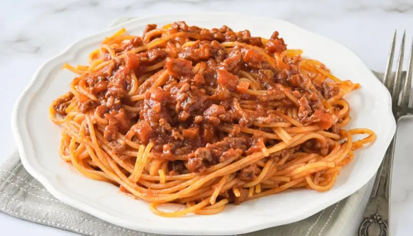 Un plato de espaguetis con carne picada, cubierto con una rica salsa de tomate y trozos de carne.