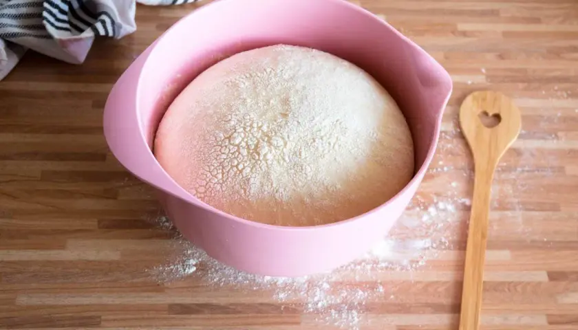 Hefeteig in rosa Schüssel, bereit für ein Osterkuchen Rezept. Holzkochlöffel mit Herzform daneben.
