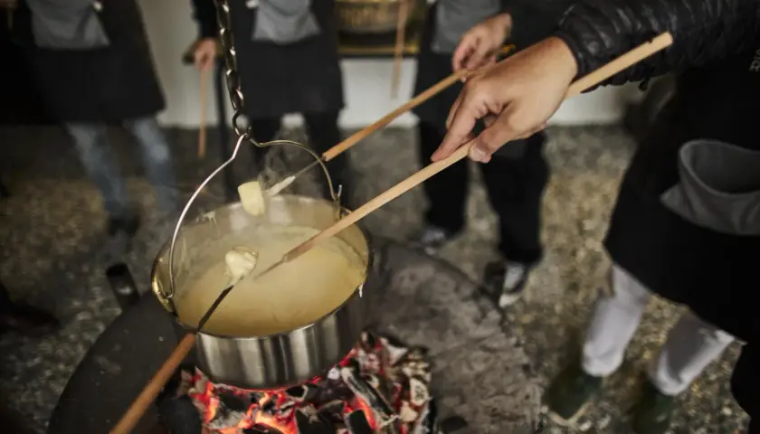 Des morceaux de pain trempent dans un caquelon de fondu suisse fumant, chauffé au-dessus d'un feu de bois.