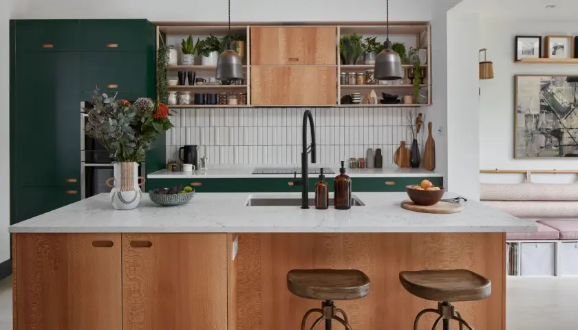 A modern kitchen island with wood grain cabinets and a white countertop, showcasing thoughtful kitchen styling with plants, fruit, and decorative items.