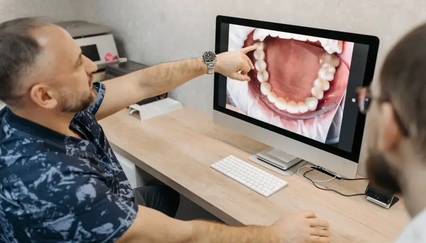 Dentysta pokazuje pacjentowi na monitorze zdjęcie jamy ustnej, wskazując na problem, jak boli kieszonka dziąsłowa.
