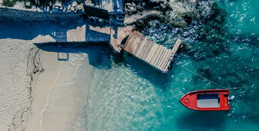 Traumhafte reiseziele august: Sandstrand, Holzsteg und ein rotes Boot im türkisfarbenen Meer. Perfekt für einen entspannten Urlaub.