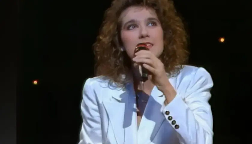 Celine Dion w białej marynarce śpiewa do mikrofonu, przypominając jej występ na Eurowizji.