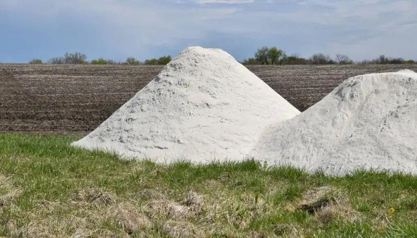 Zwei große Haufen weißes Material, vielleicht Kalkstickstoff, liegen auf einem Feld. Der **Kalkstickstoff Verbot** könnte die Ursache für diese Lagerung sein.